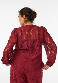 Bordeaux blonde top med blomster mønstre, lange puffede ærmer og rund halsudskæring. Gennemsigtig design med tekstureret detaljering gennem hele toppen.