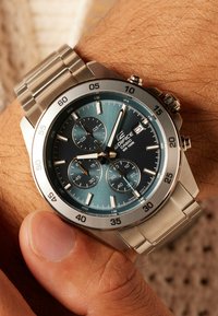 Silver stainless steel watch with a blue gradient dial, three subdials, and luminous markers. Stopwatch function and textured bezel details.