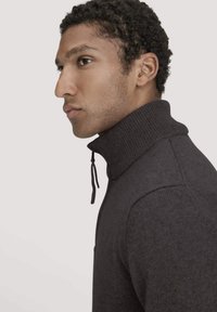 Dunkelgrauer Strickpullover mit hohem Kragen, schmaler Passform, gerippten Details und verstellbarem Kordelzug am Hals.