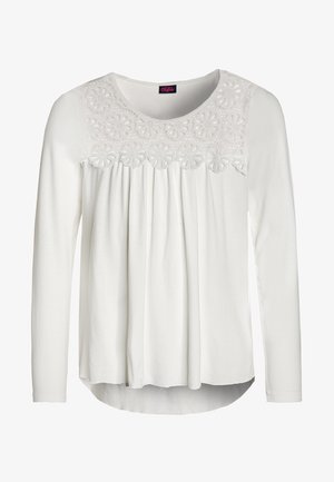 Biała bluzka z długim rękawem, okrągłym dekoltem, koronkową wstawką kwiatową na karczku oraz pionowymi plisami poniżej karczka z przodu.