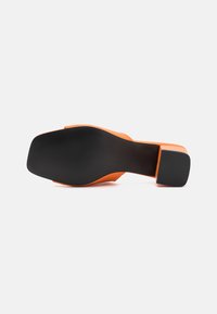 Sandal de tacón alto naranja con tacón bloque, que presenta una textura suave y una suela de goma negra. Diseño de punta cuadrada y estilo minimalista.