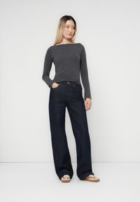 Tamno plave široke traperice u kombinaciji s dugim sivim topom. Outfit je upotpunjen svijetlim cipelama s dekorativnim detaljima.