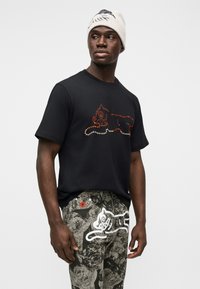 Μαύρο βαμβακερό t-shirt με κόκκινο και πορτοκαλί σχέδιο από στρας. Συνδυασμένο με γκρι παντελόνι με μοτίβο, που απεικονίζει λευκή γάτα.