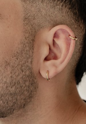 Gold hoop earrings are worn in the earlobe and cartilage, featuring a smooth, shiny surface and a simple, classic design.