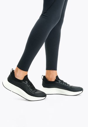 Black athletic shoes with a textured mesh upper and white midsole. Features a sock-like collar and smooth laces for secure fit.