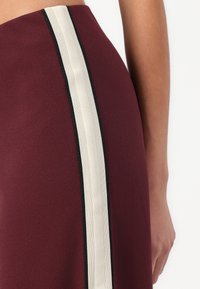 Jupe bordeaux avec une rayure blanche verticale bordée d'accents noirs, fabriquée dans un tissu lisse avec une coupe ajustée.