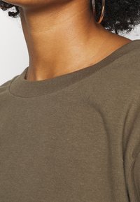 Camiseta de algodón verde oliva con cuello redondo y mangas cortas, que presenta una textura suave y un corte regular.