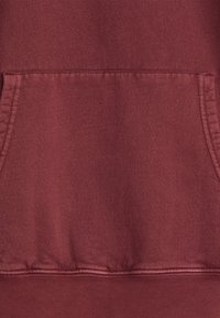 Burgundy sweatshirt with a textured knit, featuring a front pocket and ribbed hem. Seam details are visible along edges.