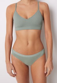 Bralette verde a coste con sottili spalline regolabili, abbinato a slip bikini a vita bassa coordinati con una cintura a rilievo. Realizzato in morbido cotone.