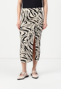 Gebreide midi-skirt met zwart en beige zebra print, voorzien van een zijsplit en gerimpelde details aan de voorkant. Zacht, textuurstof.