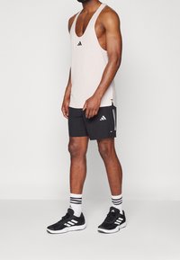 Vaaleanpunaista hihattomaa toppia, jossa on musta Adidas-logo, yhdistettynä mustiin shortseihin, joissa on valkoisia yksityiskohtia, sekä mustiin urheilukenkiin, joissa on raitoja.