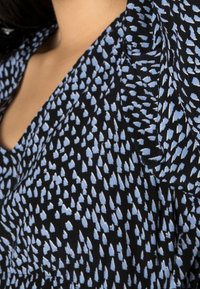 Musta kangas, jossa on kuvio, joka koostuu hajanaisista vaaleansinisen sävyisistä lehtiä tai pisaroita muistuttavista muodoista ja pehmeä, virtaava ulkonäkö.