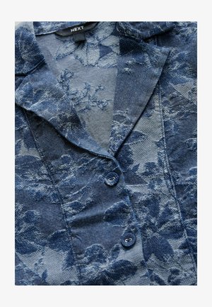 Chemise en denim bleu avec texture florale, dotée d'un col à encoches et de deux boutons. Tissu doux dans des tons de bleu foncé et clair.