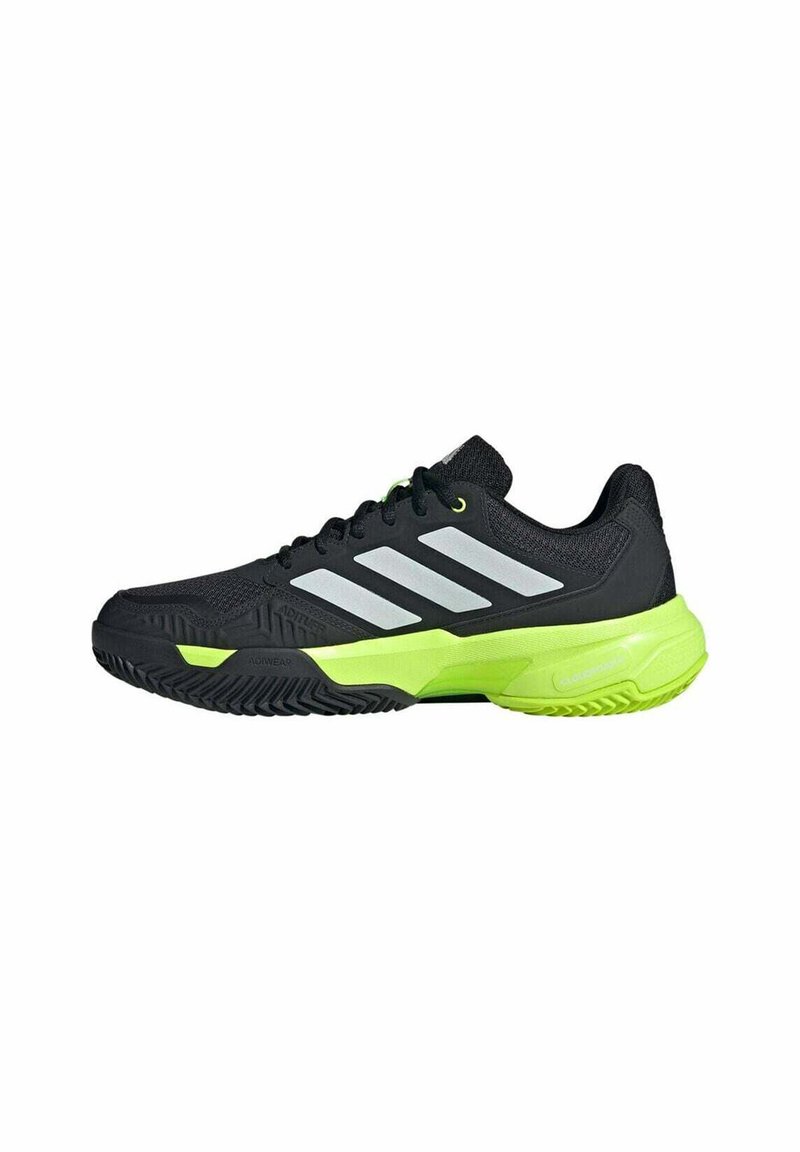 Chaussure de sport noire avec des accents verts, présentant un dessus texturé, trois rayures argentées et une semelle en caoutchouc durable avec un motif de traction.