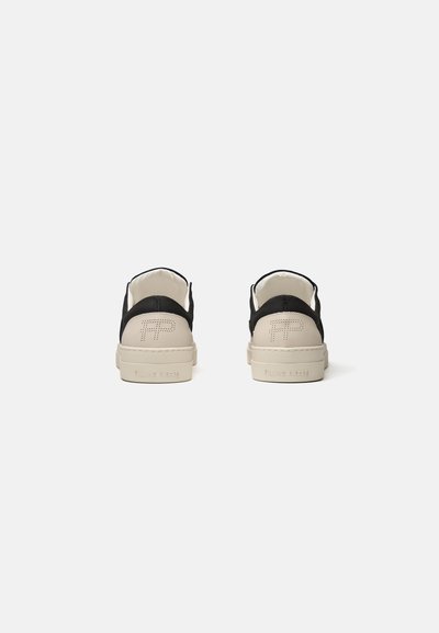 Para niskich sneakersów z białymi podeszwami i czarnymi detalami z tkaniny, widziana od tyłu na jednolitym białym tle.