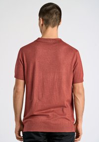 Röd kortärmad pikétröja med texturerad stickning, en platt krage och rak nederkant, med subtila ribbade detaljer vid kragen och ärmarna.