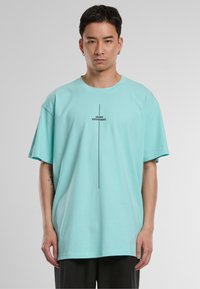 Tricou supradimensionat din bumbac de culoare bleu deschis, cu mâneci scurte, având textul "I THINK DIFFERENT." tipărit vertical în negru.