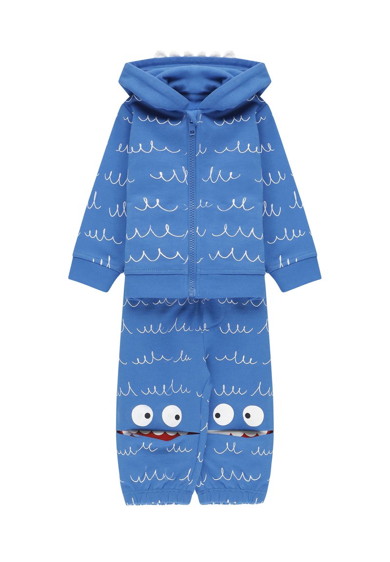 Felpa blu con zip e pantaloni abbinati realizzati in tessuto morbido, caratterizzati da motivi a onda e occhi di cartone con accentuazioni rosse sulle gambe inferiori.