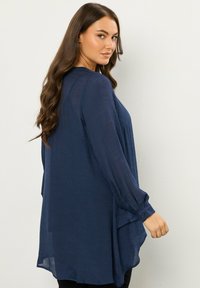 Blusa a maniche lunghe blu navy realizzata in tessuto leggero, con una vestibilità ampia, una texture sottile e un orlo leggermente curvo.