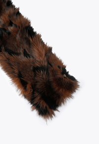 Écharpe en fausse fourrure marron et noire avec une surface douce et texturée et une extrémité arrondie. Présente un accent décoratif en métal.