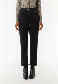 Black denim jeans with a fitted design, front pockets, and a button closure. Paired with black pointed toe heeled boots.