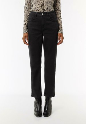 Schwarze Jeans aus Denim mit einer figurschmeichelnden Passform, Fronttaschen und einem Knopfverschluss. Kombiniert mit schwarzen Stiefeletten mit spitzer Zehenform und Absatz.