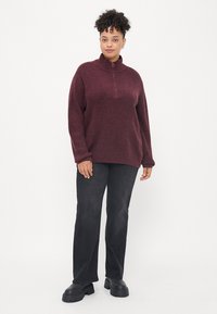 Jersey burdeos con cuello de media cremallera. Corte holgado, tejido texturizado. Combinado con pantalones negros de pierna recta y botas negras gruesas.