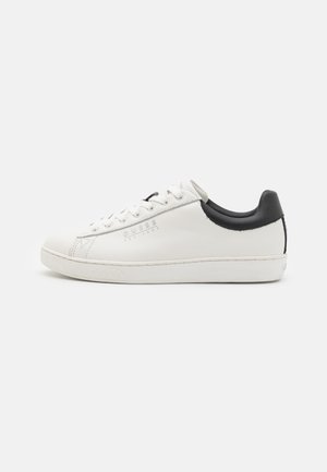 White leather sneaker with a black heel accent, round toe, and flat rubber sole. Features logo detailing and standard lace-up closure.