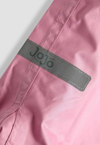 Rožinė, sintetinė medžiaga su lygiu paviršiumi. Yra pilkas etiketas su "JoJo" prekės ženklu ir kontrastinga siuvimo linija palei siūles.