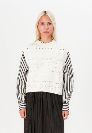Hvit strikket crop-genser med teksturerte mønstre og åpningsarbeid. Laget over et svart plisserte skjørt med vertikale hvite striper.