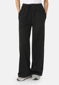 Black wide-leg pants with a drawstring waist, made of soft fabric, featuring side pockets and a smooth texture. Accented with minimal hardware.