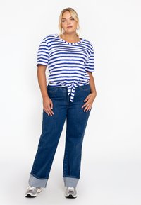 Blaue und weiße gestreifte T-Shirt mit kurzen Ärmeln und einem geknoteten Frontteil, kombiniert mit dunkelblauen Jeans mit umgeschlagenen Säumen.