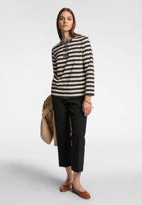 Camicia a maniche lunghe a righe beige e nera con bottoni decorativi, abbinata a pantaloni neri a 3/4 e scarpe flat marroni.