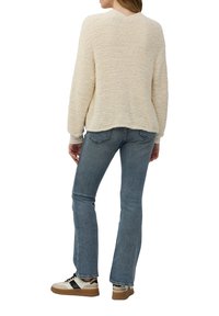 Crème gekleurde trui met een relaxte pasvorm, gecombineerd met lichtblauwe denim jeans en beige sneakers met zwarte accenten.