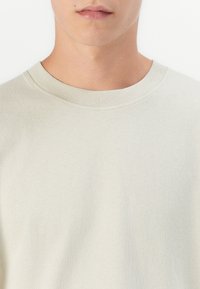 Lys beige bomulds t-shirt med klassisk rund hals og korte ærmer, der har en blød tekstur og sømløs finish.