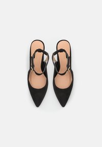 Chaussures à talons hauts en daim noir, avec un bout pointu, un design slingback et un accent chaîne dorée sur les brides. Semelle intérieure beige lisse.