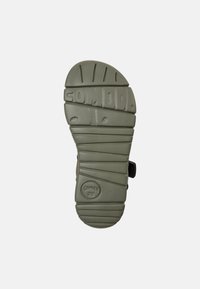 Πράσινη καουτσούκ σόλα παπουτσιού με υφή που προσφέρει πρόσφυση, με στρογγυλεμένες άκρες, αρθρωτά σχέδια και ανάγλυφη επωνυμία στην επιφάνεια.