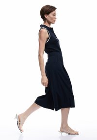 Mono sin mangas de color navy con cuello tipo polo, cuenta con ribete blanco y un botón en la parte frontal. Combinado con sandalias de tacón blanco con tiras.