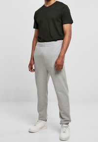 Ciemnozielona koszulka i jasnoszare spodnie dresowe z elastycznym paskiem, połączone z białymi butami sportowymi. Casualowy strój odpowiedni do relaksu.