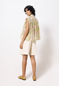 Bloemmotief, lichtgewicht stoffen top met een geplooid ontwerp, gecombineerd met lichte, knielange shorts en gele leren schoenen.