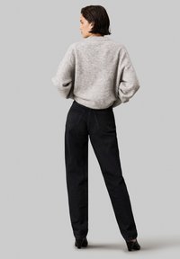 Suéter gris de punto con hombros caídos, combinado con unos jeans negros de cintura alta. La vista trasera muestra la forma de las piernas y sutiles detalles en los bolsillos.