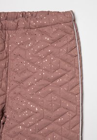 Gequilte bruine broek met een geometrisch patroon, voorzien van metalen accenten en een witte streep langs de zijkant, elastische tailleband.