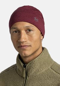 Man wearing a maroon beanie with Buff logo and an olive green fleece jacket with a zippered collar, neutral background.