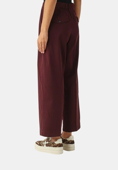Pantaloni bordeaux a gamba larga con vita elasticizzata e tasca posteriore, abbinati a sneaker platform con stampa leopardata. Tessuto dalla texture liscia.