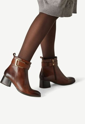 Braune Leder-Stiefeletten mit Blockabsätzen, seitlichen Reißverschlüssen und Schnallenriemen, getragen mit dunklen Strumpfhosen und einem grauen gestrickten Rock.
