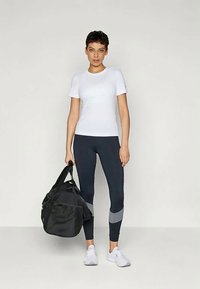 Valge sobiv T-särk, tumesinised retuusid hallide aktsentidega, must spordikott ja valged tossud. Sile kangas, sportlik lõige, minimaalne disain.