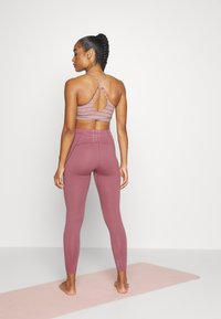Tajmat sportbehå med ett mönstrat design och korslagda remmar på baksidan, tillsammans med högmidjade, enfärgade rosa leggings med en slät textur.