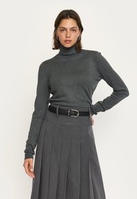 Grijze coltrui met een geribbelde textuur, gecombineerd met een hooggewaisted grijze plissérok en een zwarte riem met een zilveren gesp.