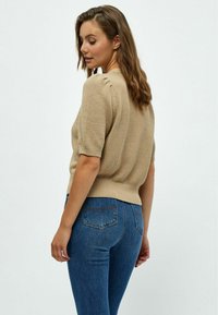 Beige Strickpullover mit kurzen Ärmeln, strukturierter Stoff und eng anliegendem Saum. Kombiniert mit blauen Jeans mit klassischem Gesäßtaschendesign.
