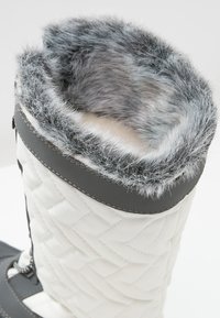Bota acolchada blanca con puño de pelo sintético gris y acentos de cuero negro, con una suela resistente y diseño de cordones para un ajuste seguro.